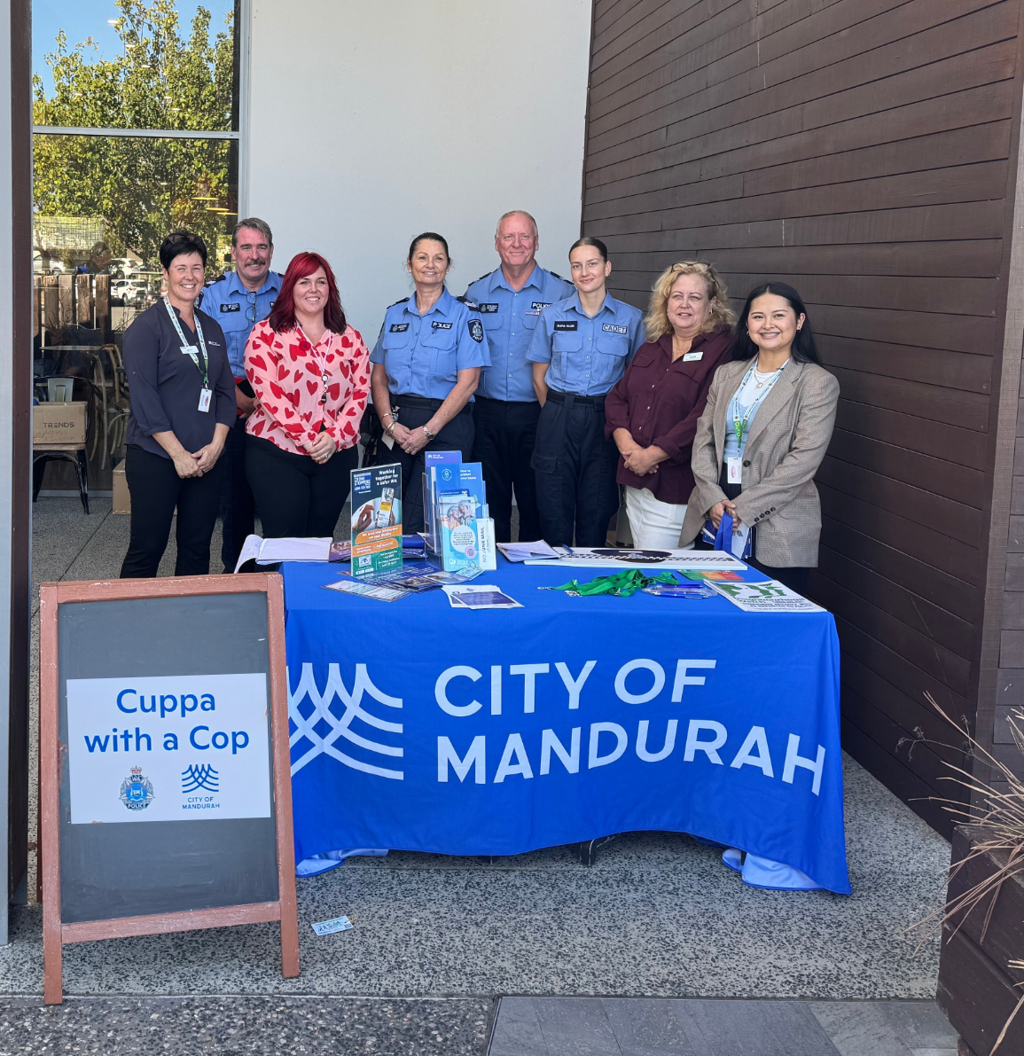 Three police officers and City of Mandurah Community Development staff standing behind a City of Mandurah branded table at a local coffee shop.